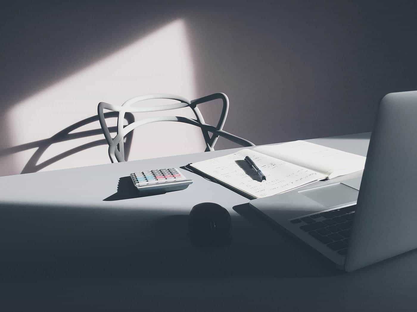 A laptop computer on a desk beside a calculator